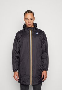 Veste imperméable noire avec fermeture éclair sur le devant, accents jaunes et bleus, capuche ajustable par cordon et poignets élastiques. Tissu léger et design mi-long.