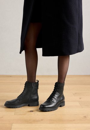 Bottes chevilles en cuir noir à finition texturée, avec lacets sur le devant et fermeture éclair latérale. Semelle épaisse et languette à l'arrière.