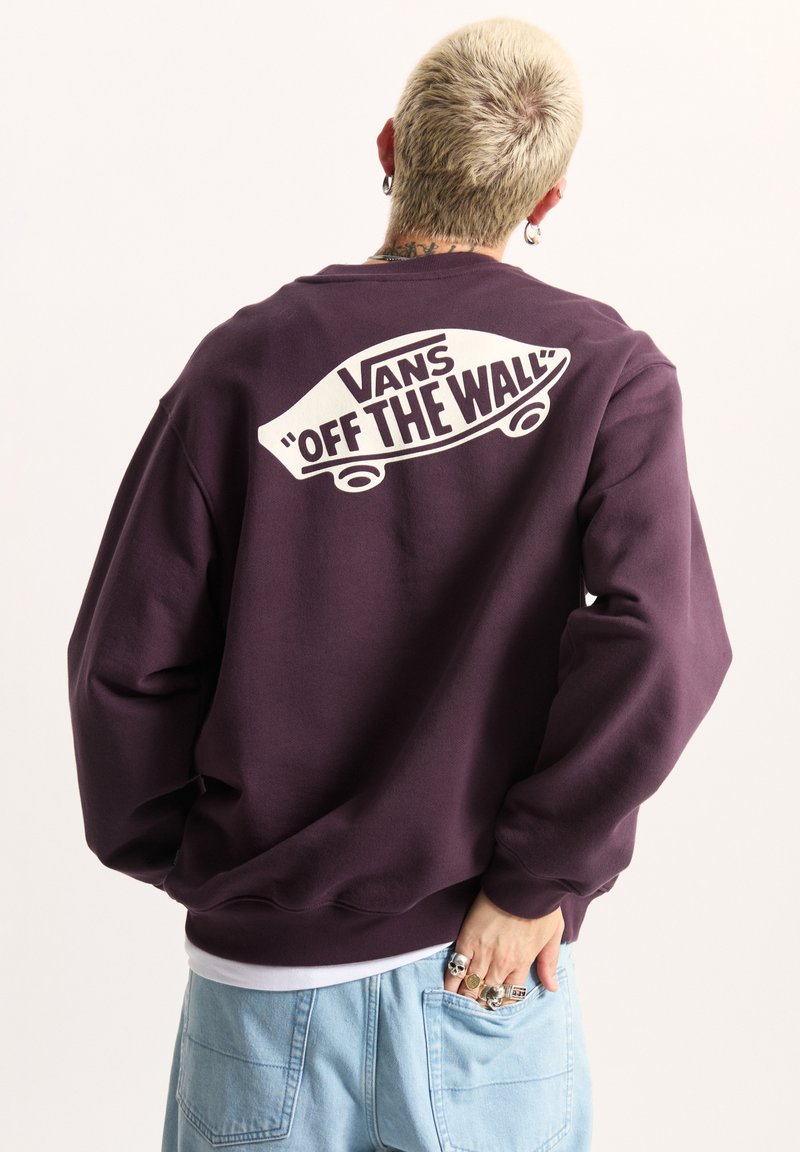 Fioletowa bluza z dużym białym logo "Vans 'Off the Wall'" z tyłu. Luźny krój z ściągaczami przy rękawach i miękką teksturą.