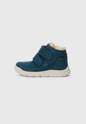 Teal waterproof ankle boots with Velcro straps, cream faux fur lining, and white rubber soles. Features a logo on the side.
