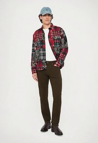 Rød og svart rutete flanellskjorte med paisley-detaljer, hvit t-skjorte, olivengrønne bukser og svarte støvler, toppet med en lyseblå caps.