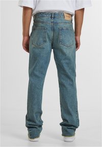 Šviesiai mėlynos džinsinės kelnės su tiesiu siuvimu, turinčios dvi užpakalines kišenes ir odinį logotipą ant juosmens. Plėšyti apvadu detalės.