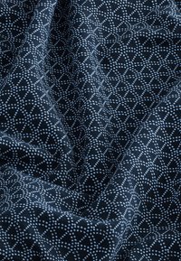 Geometriai mintájú szövet kék és világoskék pöttyökkel sötétkék háttéren, sima tapintású, redőzve, hogy bemutassa a mélységet és hajtásokat.