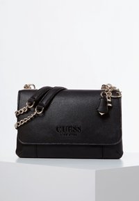 Sort tekstureret faux læder crossbody taske med flaplukning, guldfarvet kædesti og brandlogo præget på forsiden.