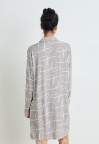 Srajčna obleka z dolgimi rokavi iz svetlo sivo tkanino, ki vsebuje bel vzorec medsebojno prepletenih zank. Oblikovanje ima ovratnik in je nekoliko široko.