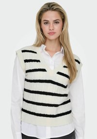 Sleeveless cream knitted vest with black horizontal stripes, featuring a V-neck and textured pattern, worn over a white collared shirt.
