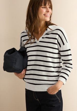 Striped knit sweater in white and black, featuring a V-neck, 3/4 sleeves, ribbed cuffs, and a textured fabric. Paired with a dark bag.
