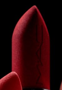 Rossetto rosso con punta appuntita, finitura opaca e logo in rilievo. Presenta una consistenza morbida e forma cilindrica. Lo sfondo è nero.