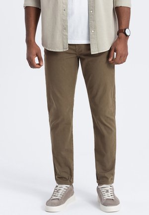Chinos caqui de tela ligera, ajuste recto, con bolsillos frontales. Combinados con zapatillas de gamuza grises, cordones blancos y una camisa de botones.