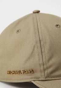 Cappellino da baseball beige realizzato in tessuto testurizzato, con un logo "Michael Kors" in oro goffrato sul lato e un design a corona arrotondata.