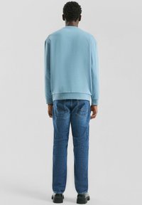 Jasnoniebieska bluza z prążkowanymi mankietami i dołem, zestawiona z ciemnoniebieskimi dżinsami z tylnymi kieszeniami i prostą nogawką. Czarne buty.
