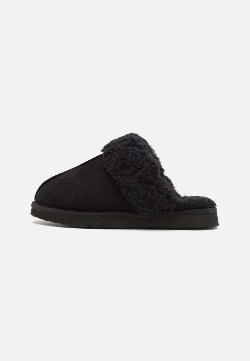 Chausson noir à enfiler avec une épaisse doublure en polaire pelucheuse et une semelle épaisse, présenté en profil latéral sur un fond blanc.