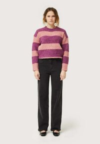 Suéter de punto esponjoso a rayas moradas y rosas con un diseño corto, mangas largas y un escote redondo, combinado con pantalones negros de cintura alta.