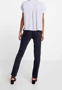 Bluzka w paski z krótkim rękawem o luźnym kroju, zestawiona z dopasowanymi granatowymi spodniami i czarnymi sandałami na obcasie, widziana od tyłu.