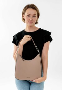 Beige leather shoulder bag with a smooth texture, curved design, and silver hardware. Bag held by a person wearing a black top.