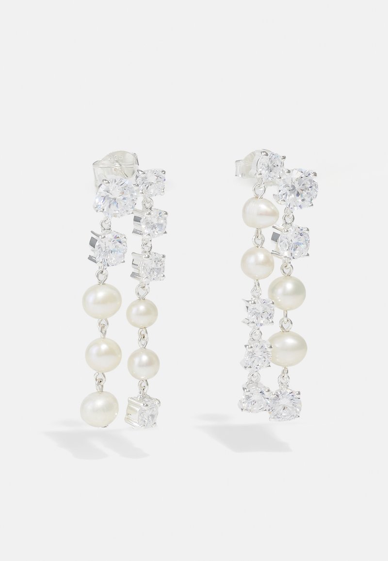 Lašeliniai auskarai, pagaminti iš sidabro metalo, su pakaitomis baltomis perlų karoliukais ir skaidriais kristalais įvairiomis formomis, su kaskadinio dizaino elementais.