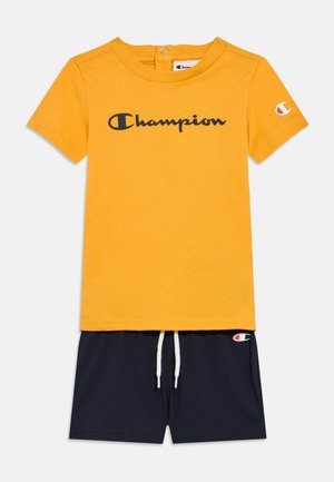 Kollane lühikeste varrukatega t-särk musta "Champion" logoga; kombineeritud tumesiniste lühikeste pükste jaotusega, millel on string ja väikene logo plakett.