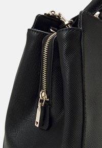 Sac à main noir avec une surface texturée, des détails de fermeture éclair dorés et un design durable. La fermeture comprend un accent distinctif en métal.