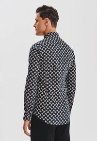 Granatowa koszula w białe kropki, z długimi rękawami i spiczastym kołnierzykiem, wykonana z lekkiego materiału.