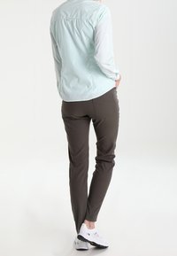 Camicia button-up azzurro chiaro con un motivo testurizzato, abbinata a pantaloni slim-fit verde oliva e scarpe da ginnastica bianche.