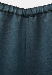 Tmavomodrý elastický pás so stredným vertikálnym švom na textúrovanej látke, pravdepodobne časť odevu alebo nohavíc.