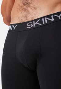 Cintura elastica nera con logo "SKINY". Il tessuto è liscio e aderente, presenta una sacca sagomata e cuciture minime per il comfort.