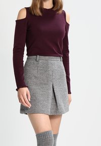 Burgunderfarbenes Shirt mit kaltem Schulterdesign und gerippter Textur, kombiniert mit einem grauen, gerippten Minirock mit einem vorderen Schlitz. Kniehohe, gerippte Socken sind enthalten.