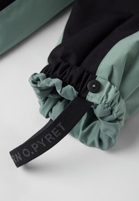 Zwart en teal stof met een gegatherde manchette, voorzien van een knoopsluiting en een zwarte band met het label "N O. PYRET." Gevarieerde kleuren en materialen.