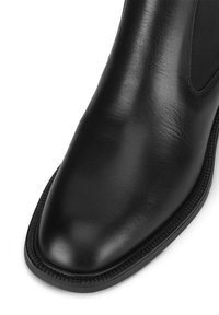 Czarne skórzane botki za kostkę z gładkim wykończeniem, elastycznymi bocznymi panelami oraz okrągłym noskiem z teksturowaną podeszwą i dekoracyjnymi przeszyciami.