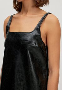 Schwarzes Kunstleder-Minikleid mit breiten Trägern, quadratischem Ausschnitt und subtiler Textur. Verfügt über ein kleines Taschendetail an der Vorderseite.