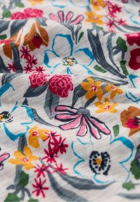 Gėlių audinys, kuriame dominuoja ryškios spalvos, įskaitant rožinę, geltoną ir mėlyną. Dizainas apima įvairius gėlių raštus ant šviesaus fono.