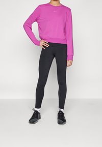Sudadera rosa de manga larga y cuello redondo, combinada con leggings negros y zapatillas deportivas negras, con un logo de Nike en blanco en la sudadera.