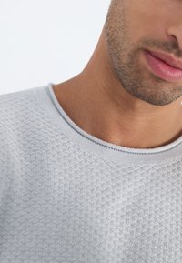 Ljusgrå texturerad sweatshirt med rund halsringning, som har ett subtilt bikake-mönster och ribbade detaljer vid kragen.