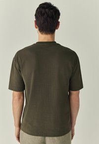 Donker groene t-shirt met korte mouwen, een ontspannen pasvorm, ronde hals en zachte katoenen textuur, getoond van de achterkant.