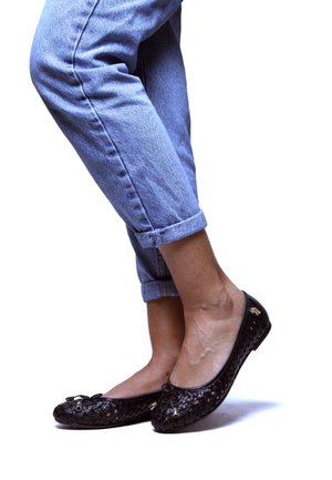 Bailarinas de tejido negro con punta redondeada, que presentan un lazo y acentos metálicos, combinadas con jeans de mezclilla azul claro con dobladillo.