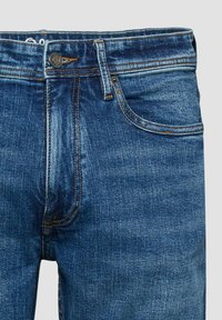 Nahaufnahme der Vorderseite blauer Jeans mit Knopf, Reißverschluss, Gürtelschlaufen und Nähten an der Vorderhosentasche.