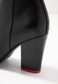 Schwarze Lederstiefelette mit runder Form, ausgestattet mit einem strukturierten Obermaterial und einem hohen, klobigen Absatz mit einem roten Akzent an der Basis.