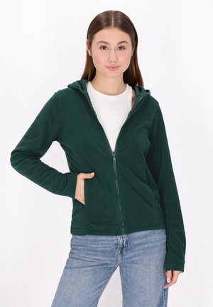 Felpa con zip di colore verde scuro, dotata di cappuccio, tasche frontali, maniche lunghe e una texture morbida; abbinata a jeans azzurri chiari.
