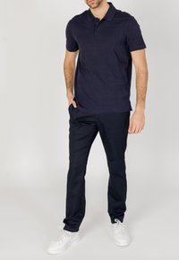 Polo shirt navy con un design testurizzato, maniche corte e colletto, abbinato a pantaloni navy e scarpe bianche. Tessuto morbido e vestibilità casual.