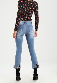 Ljusblå denim skinny jeans med fransad fåll. Kombinerat med en svart blommig långärmad topp. Modellen bär svarta högklackade stövlar.