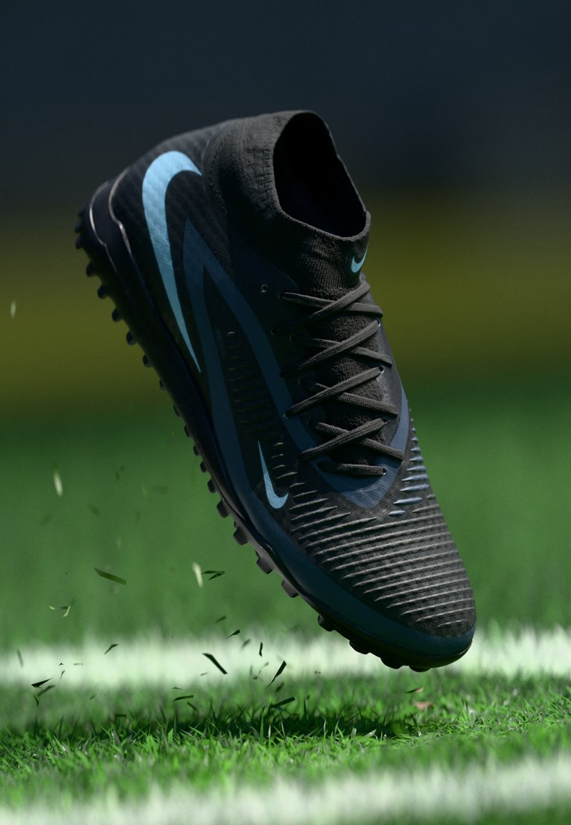 Černá fotbalová kopačka s texturovaným svrškem, modrým logo Swoosh a černými tkaničkami. Položena nad zelenou trávou s malými částečkami trávy, které se vznášejí ve vzduchu.