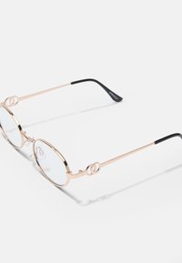 Ochelari rotunzi cu o ramă din metal roz aurie, lentile transparente și uite din plastic negru. Accente decorative pe ramă.