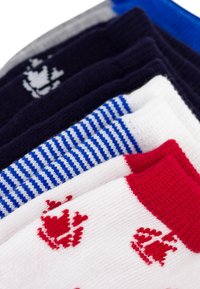 Cinque paia di calze in vari colori: blu navy, rosso, bianco e blu. Le caratteristiche includono righe, colori solidi e un motivo decorativo a forma di corona.