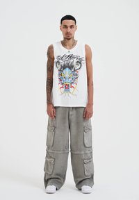 White sleeveless tank top featuring a colorful dragon graphic, paired with loose, light gray cargo pants with multiple pockets.