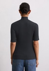 Zwarte geribbelde top met korte mouwen en hoge hals. Soepele textuur, aansluitend ontwerp, gecombineerd met blauwe spijkerbroek met achterzakken.