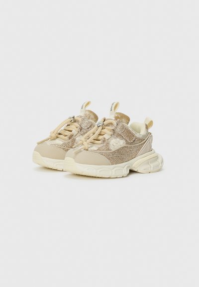 Kinderbeige Sneakers mit Glitzerakzenten, dicken weißen Sohlen, Schnürsenkeln und einem Klettverschluss auf einem weißen Hintergrund.
