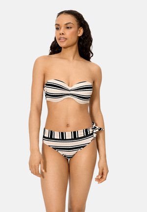 Mujer con bikini de rayas blancas y negras sin tirantes, con un detalle de lazo en el lado izquierdo de la parte inferior, posando frente a un fondo sencillo.