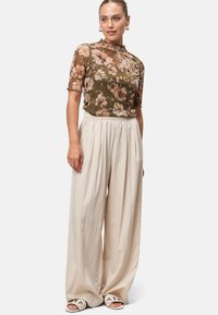 Olive green floral sheer top with short sleeves, paired with cream wide-leg trousers, showcasing relaxed fit and textured fabric.