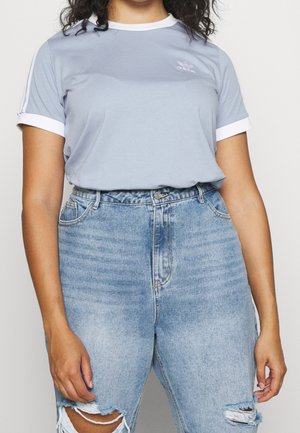 Lyseblå bomuld T-shirt med hvid krave og ærmekanter, med et lille logo på brystet. Båret med slidte blå jeans.