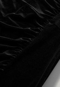 Tissu en velours noir avec un détail froncé rassemblé et un panneau lisse, mettant en valeur la texture et le contraste du matériau.